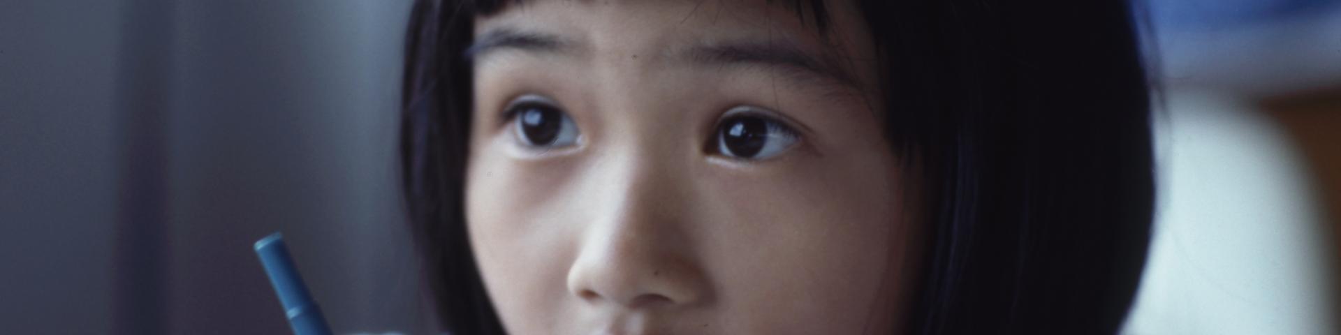 Child sitting with a pen at a desk looking up