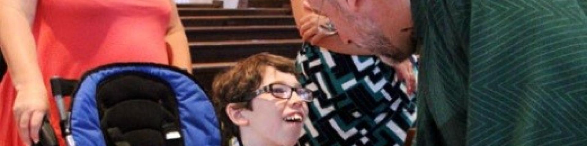 Priest shaking the hand of a child who uses a wheelchair