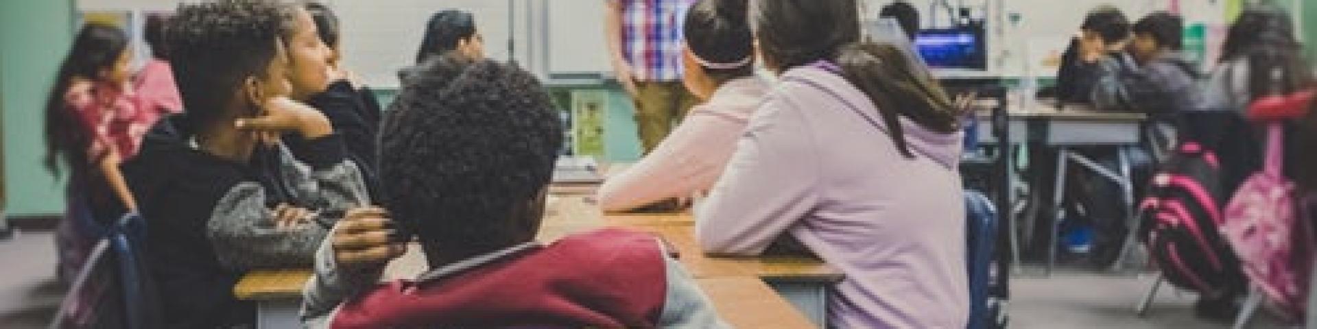 Students at their desks watching their teacher teach