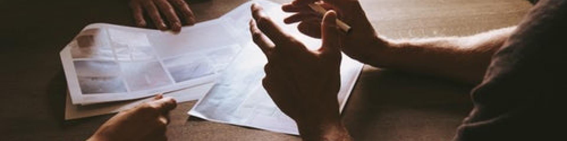 Pieces of paper on a table with three peoples hands in discussion