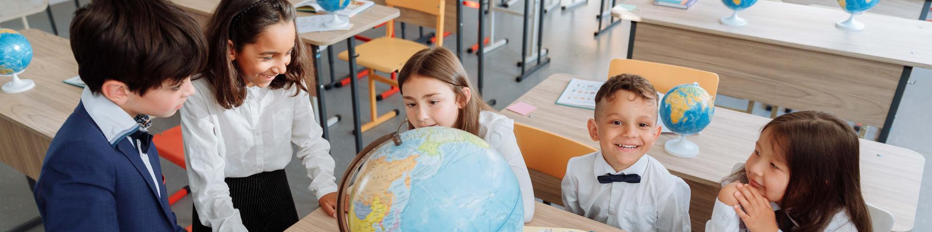 Kids in uniform looking at a globe and smiling.