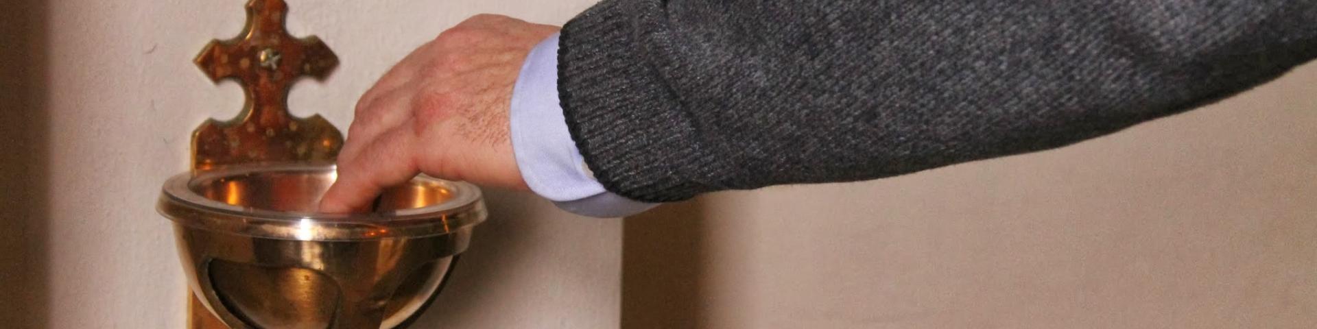 A man's hand dipped into a holy water font 