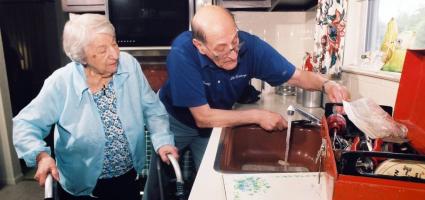 Picture of a husband helping his wife in the kitchen. Wife has a walker. 