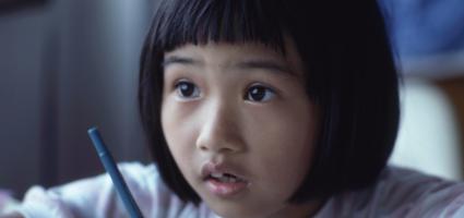 Child sitting with a pen at a desk looking up