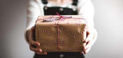 A teenage girl holding out a gift with candy cane wrapping paper