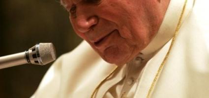 Pope John Paul II speaks into a microphone from a seated position, bent a bit.