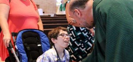 Priest shaking the hand of a child who uses a wheelchair