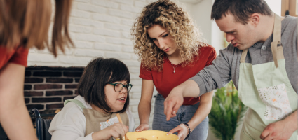 Young adults, one in a wheelchair, one with Down Syndrome, one with no visible disability, cooking.