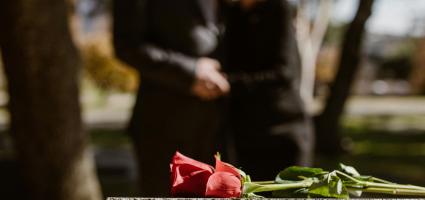 Flower on headstone with blurred image of couple in background.