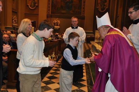 Two children handing the gifts of bread and wine to the Bishop during Mass. One of them has down syndrome.