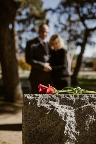 Flower on headstone with blurred image of couple in background.