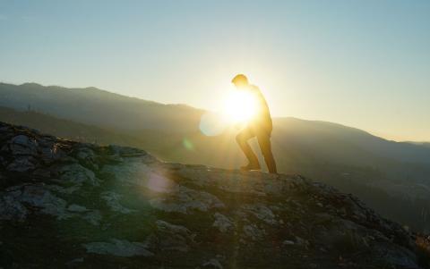 The silhouette of a person climbing on a mountain with the sun in the background