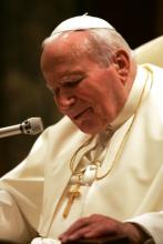 Pope John Paul II speaks into a microphone from a seated position, bent a bit.