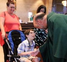 Priest shaking the hand of a child who uses a wheelchair