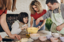 Young adults, one in a wheelchair, one with Down Syndrome, one with no visible disability, cooking.