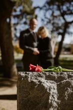 Flower on headstone with blurred image of couple in background.
