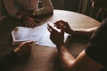 Pieces of paper on a table with three peoples hands in discussion 
