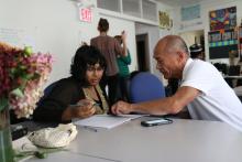 An adult male teaching working at a table with a teenage woman in a classroom